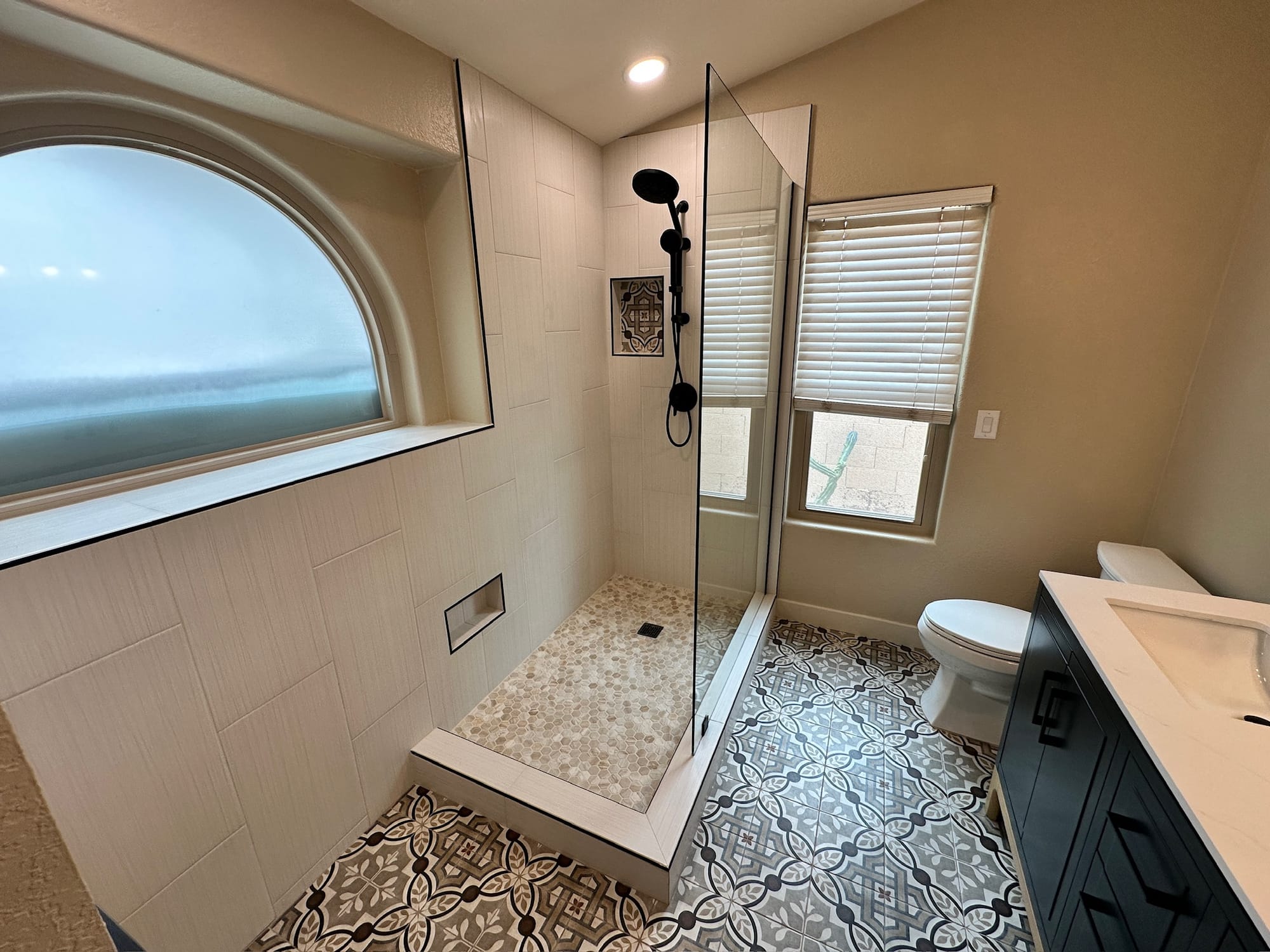 Ahwatukee master bathroom after — extended walk-in shower with vertical tile, niche, and the original arched window preserved