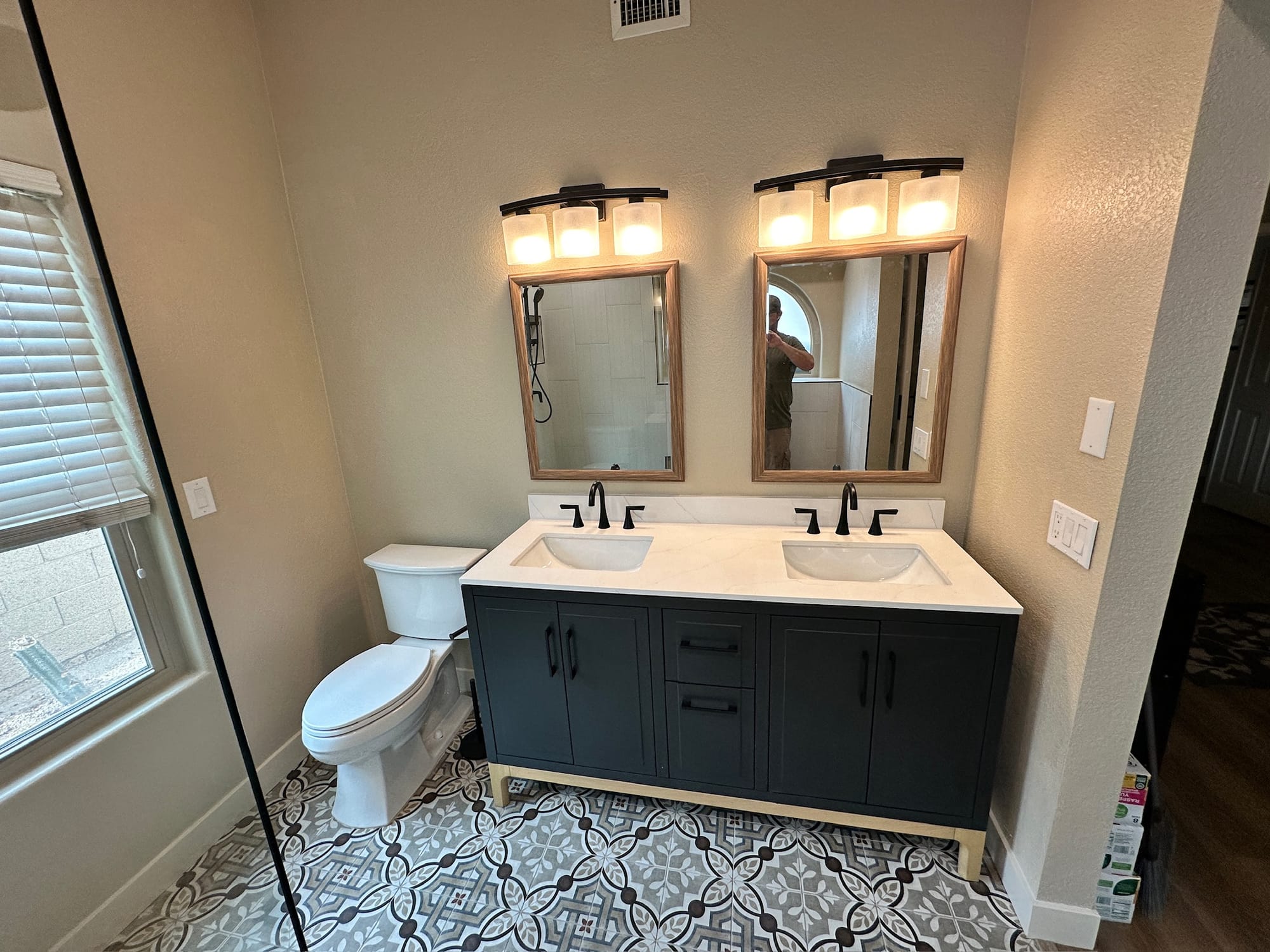 Master bathroom remodel — navy freestanding double vanity with framed mirrors, matte black fixtures, and patterned cement-look tile floor