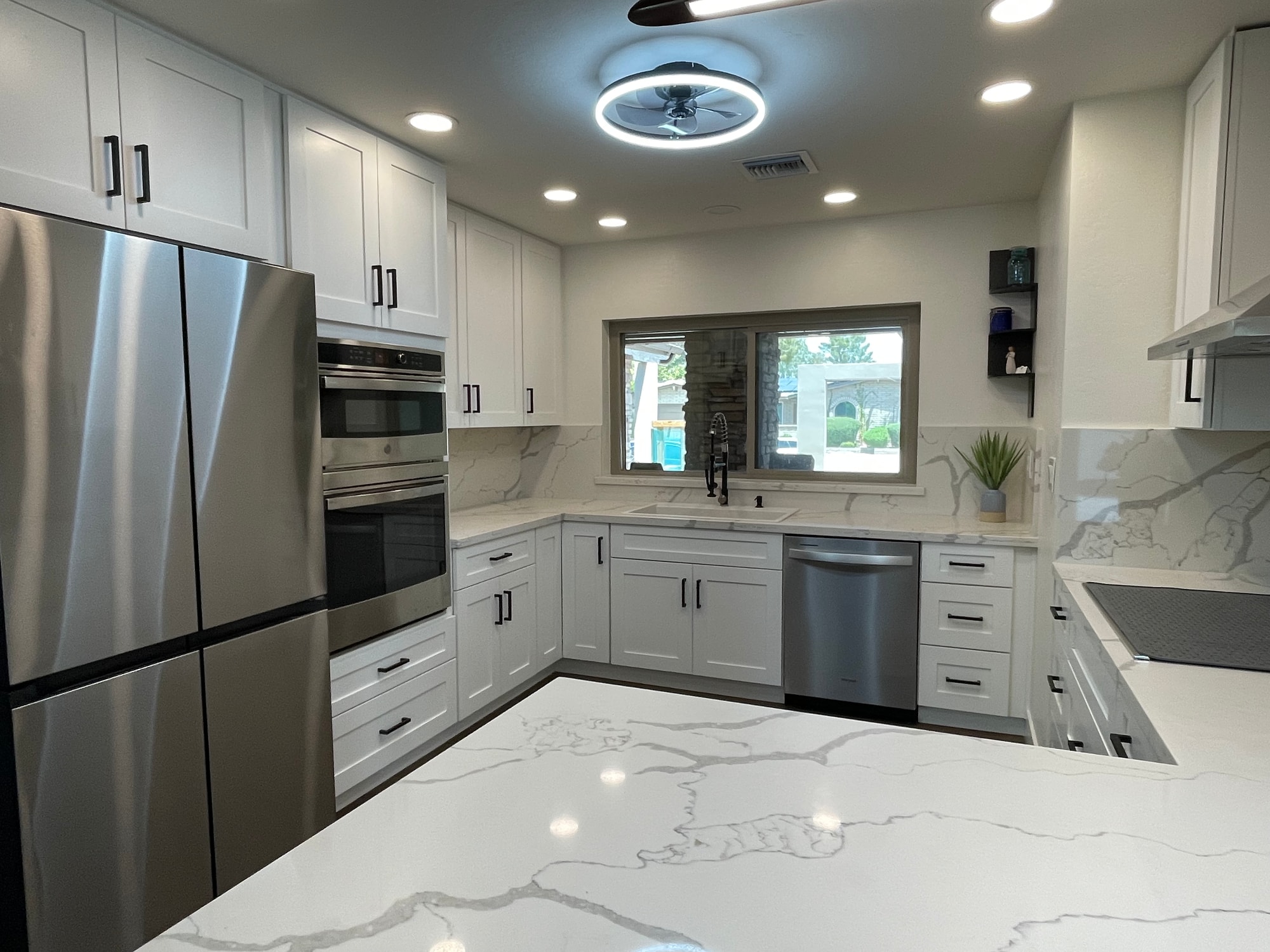 Chandler kitchen after — Sollid Three Series Shaker White cabinets, Della Terra Calacatta Divine quartz counters and full-height backsplash, stainless appliance package, matte black hardware, and 7-foot LVP planks