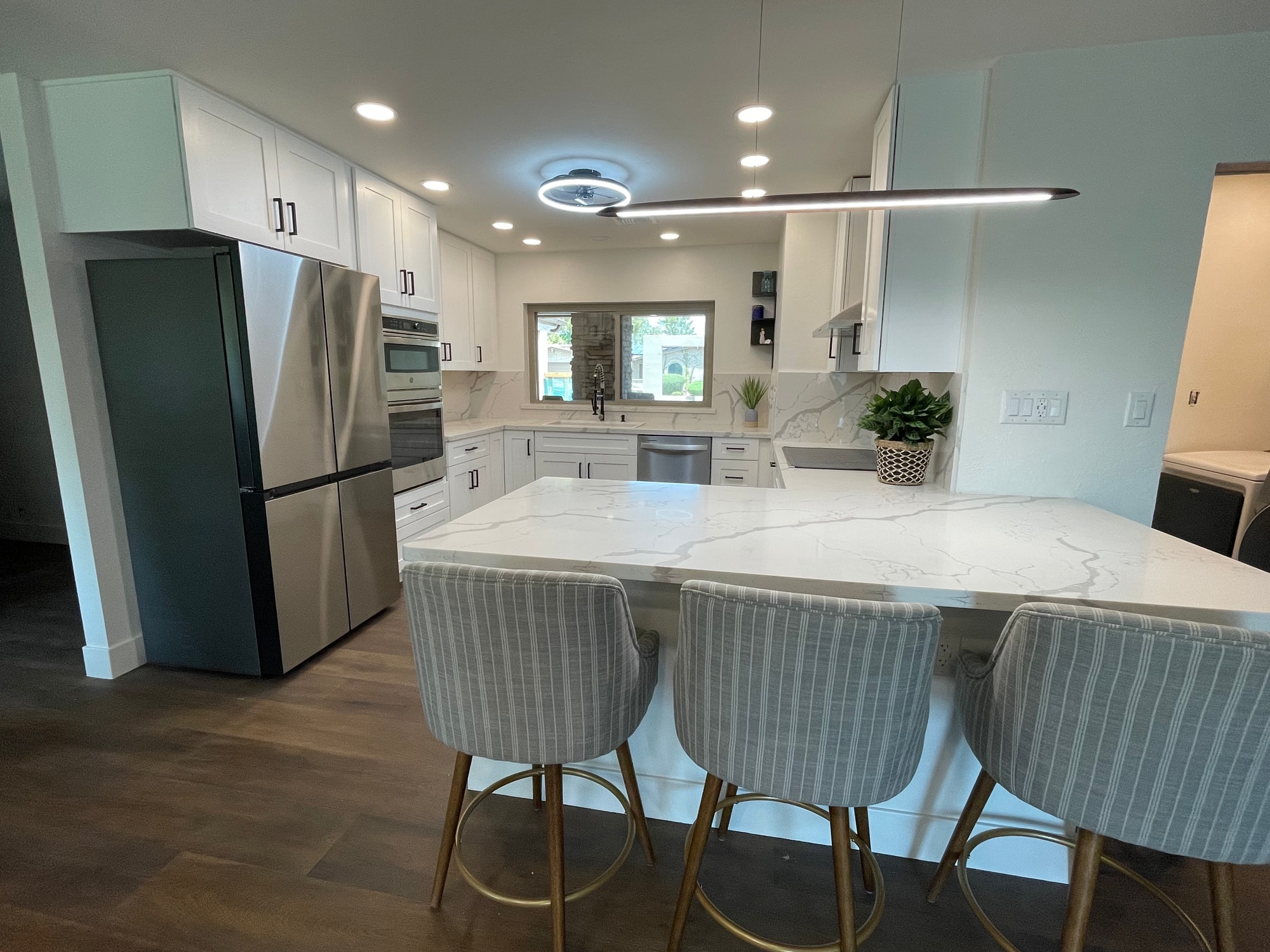 Chandler kitchen — peninsula with Calacatta Divine quartz counter, three upholstered bar stools, linear pendant above, and LED ring fan centered in the room