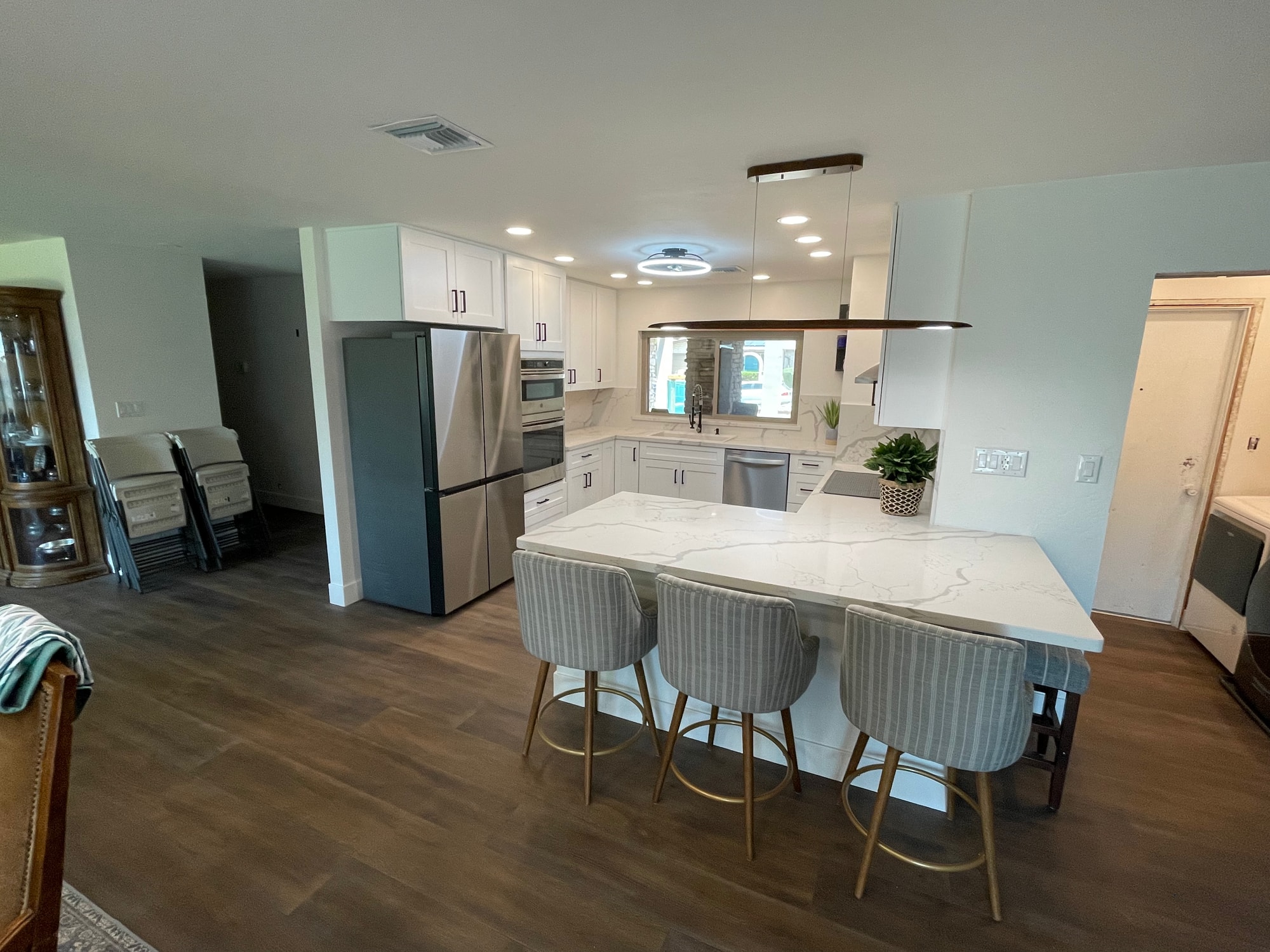 Chandler kitchen — pulled-back view showing peninsula bar seating, open flow to the dining and living areas, and 7-foot LVP planks running through the whole first floor