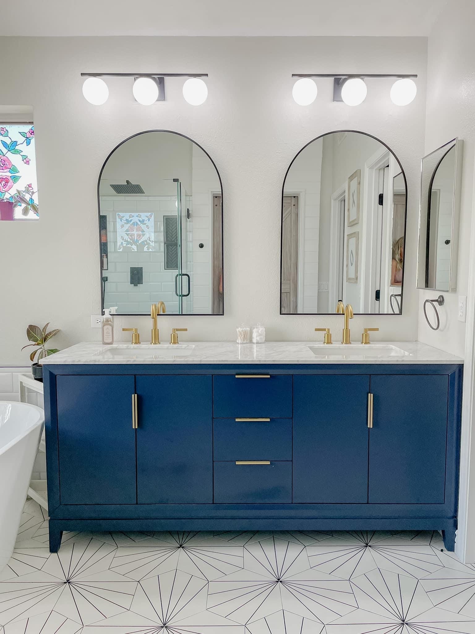 Gilbert master bathroom after — navy freestanding double vanity with arched black-framed mirrors, gold globe sconces, and polished gold faucets