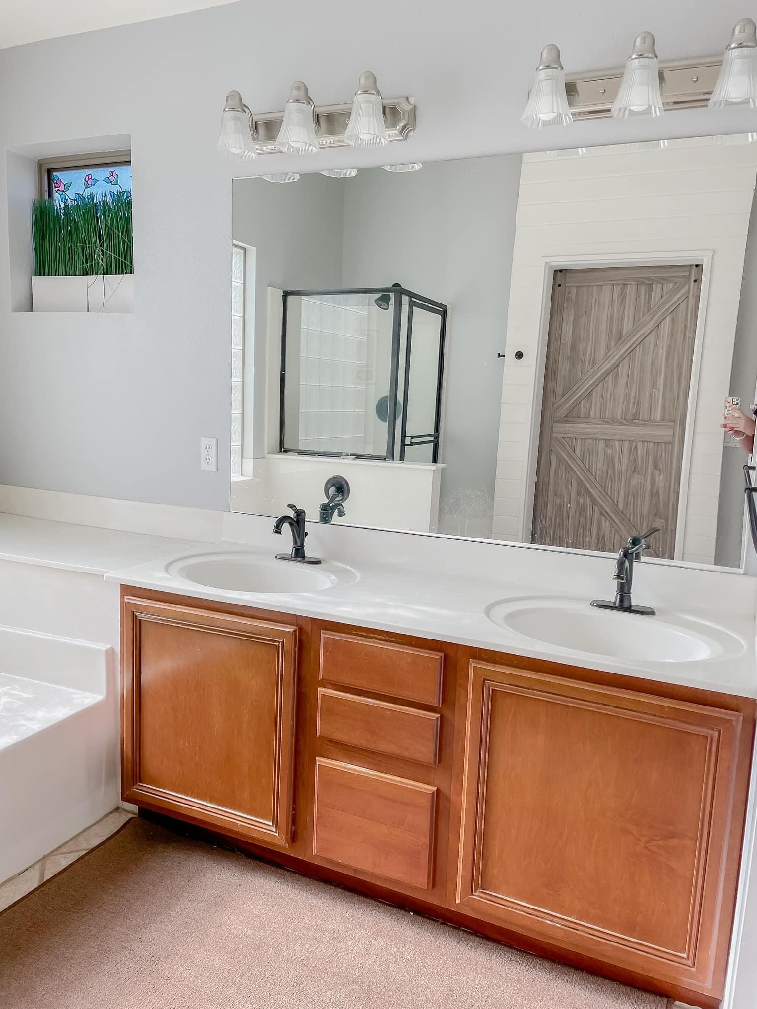 Gilbert master bathroom before — old cherry double vanity with cultured marble top, builder-grade lighting, and barn door visible behind