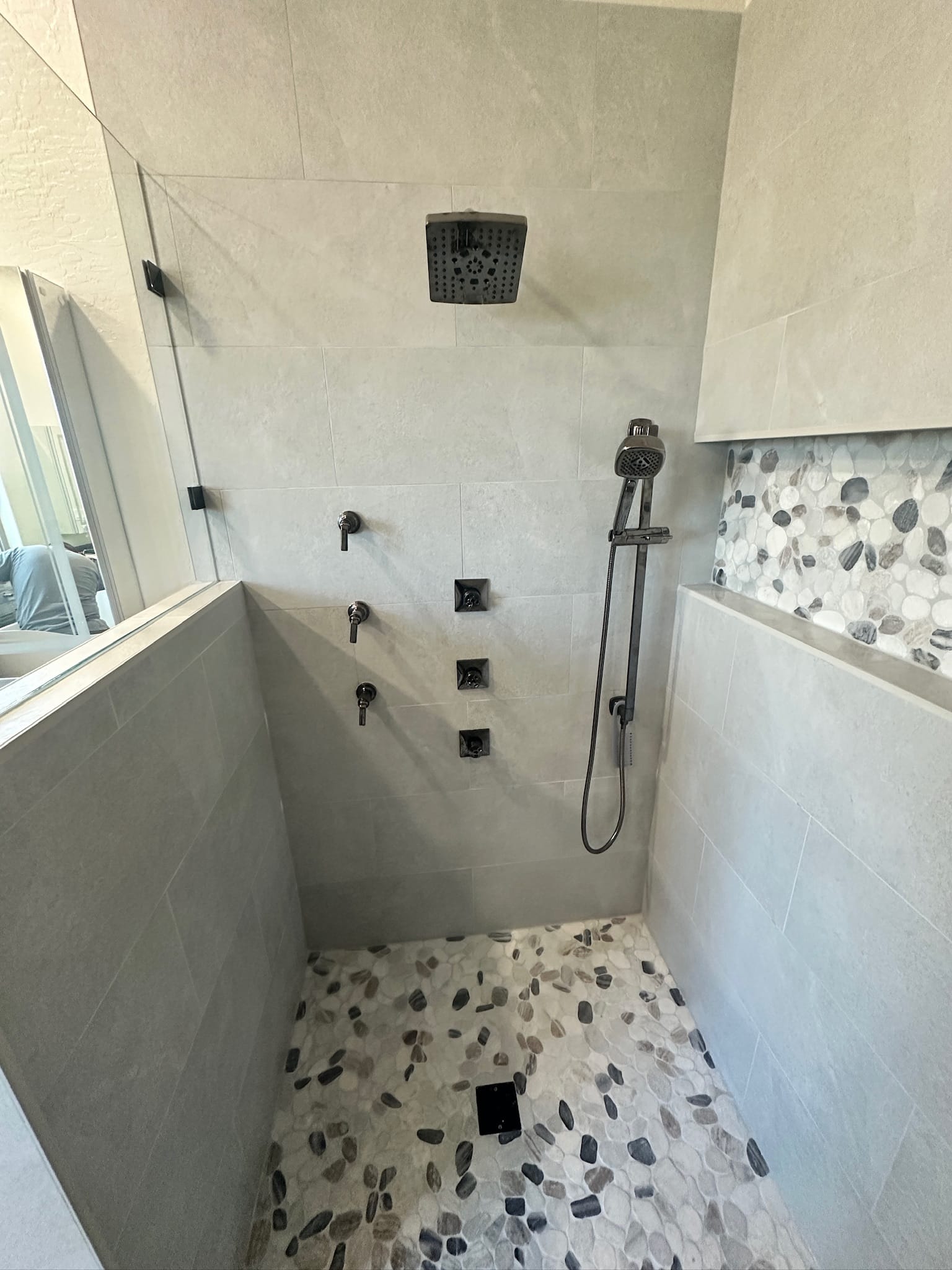 Gilbert master bathroom after — walk-in shower with large-format porcelain tile, sliced-pebble mosaic niche and floor, black Delta rain head and three body sprays