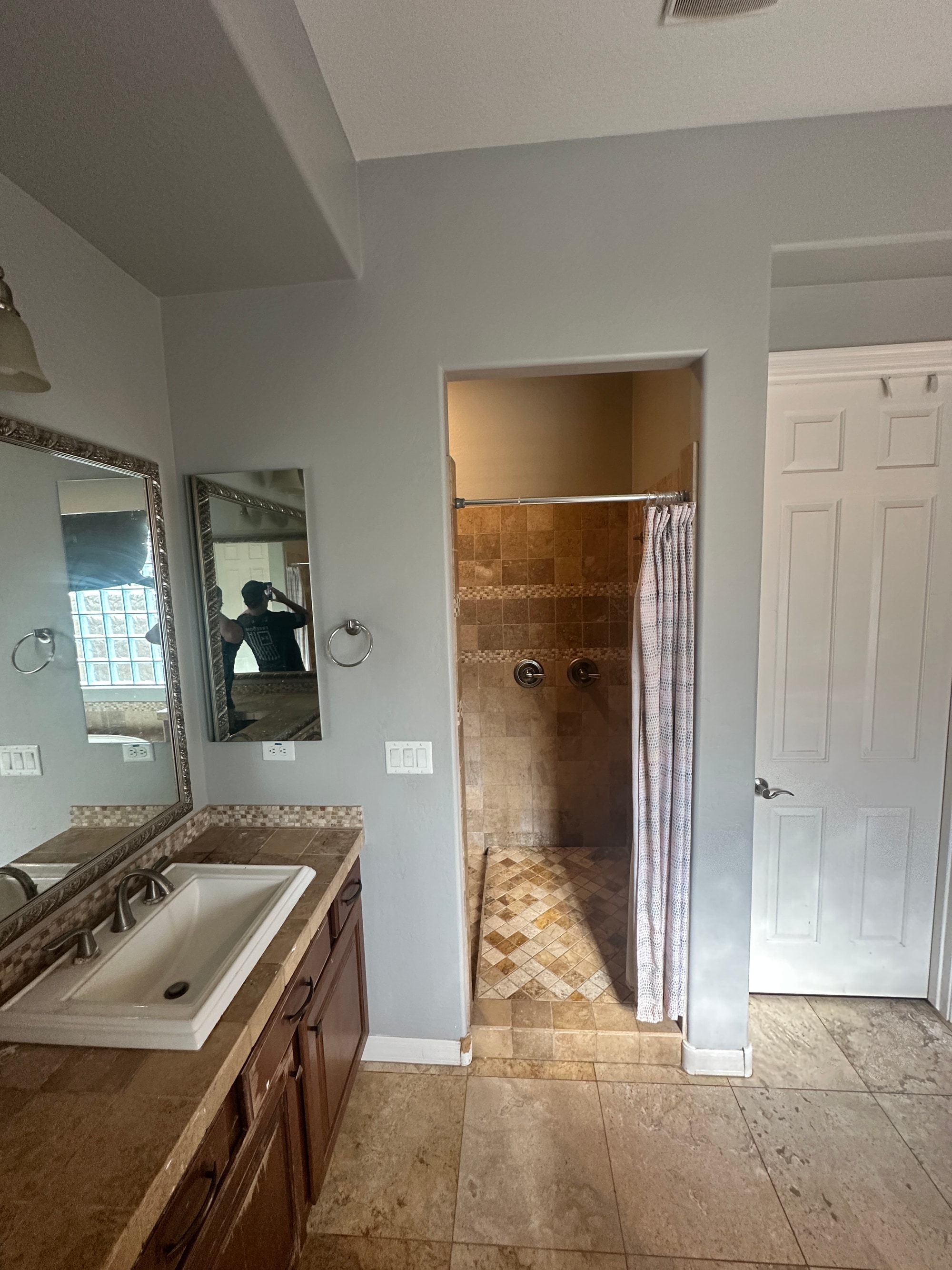 Gilbert master bathroom before — dated tan-tile shower stall with a shower curtain rod, mosaic accent stripe, and dark raised-panel vanity next to it