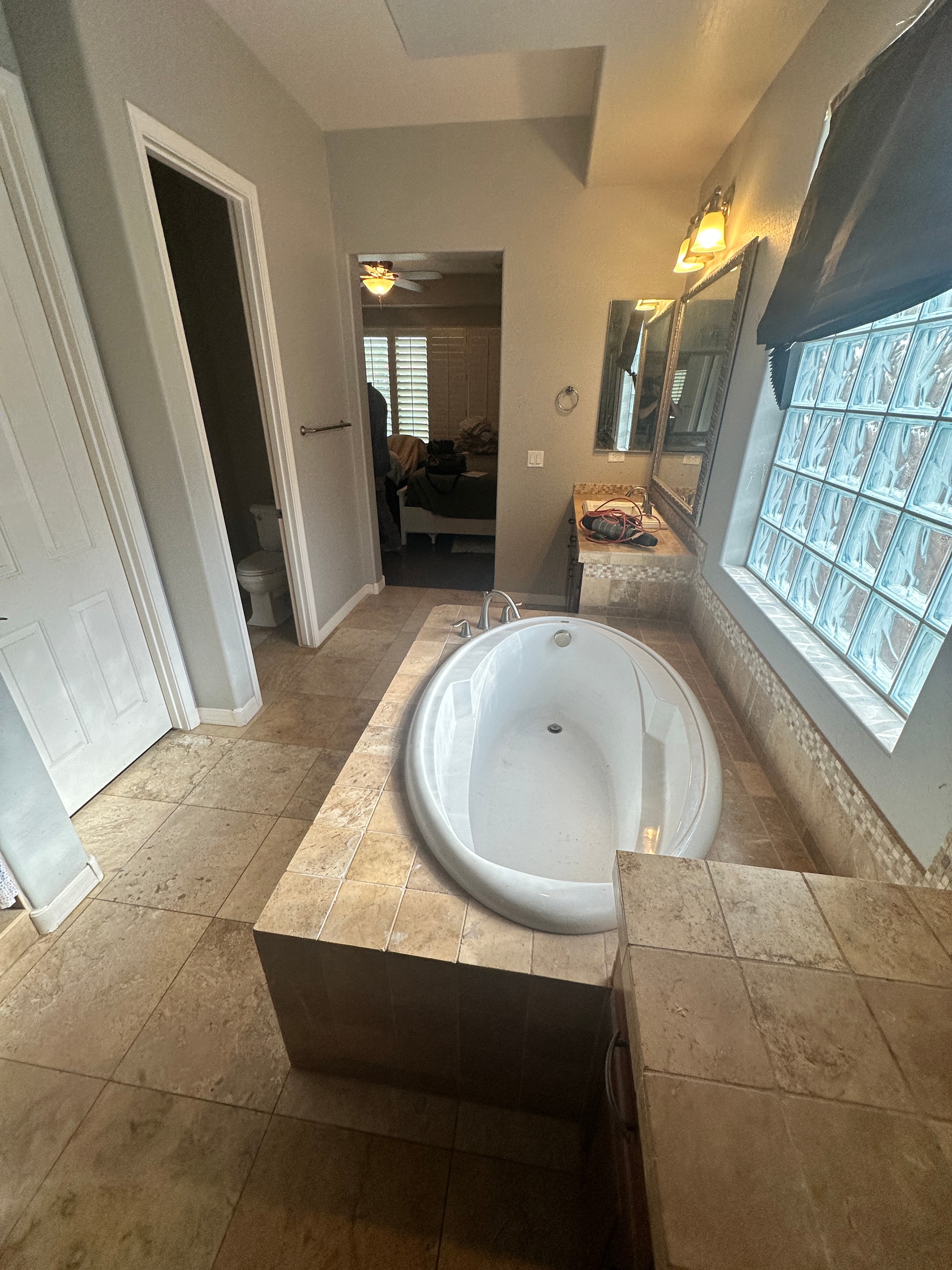 Gilbert master bathroom before — large built-in oval jetted tub in a travertine-look tile surround under a glass-block window