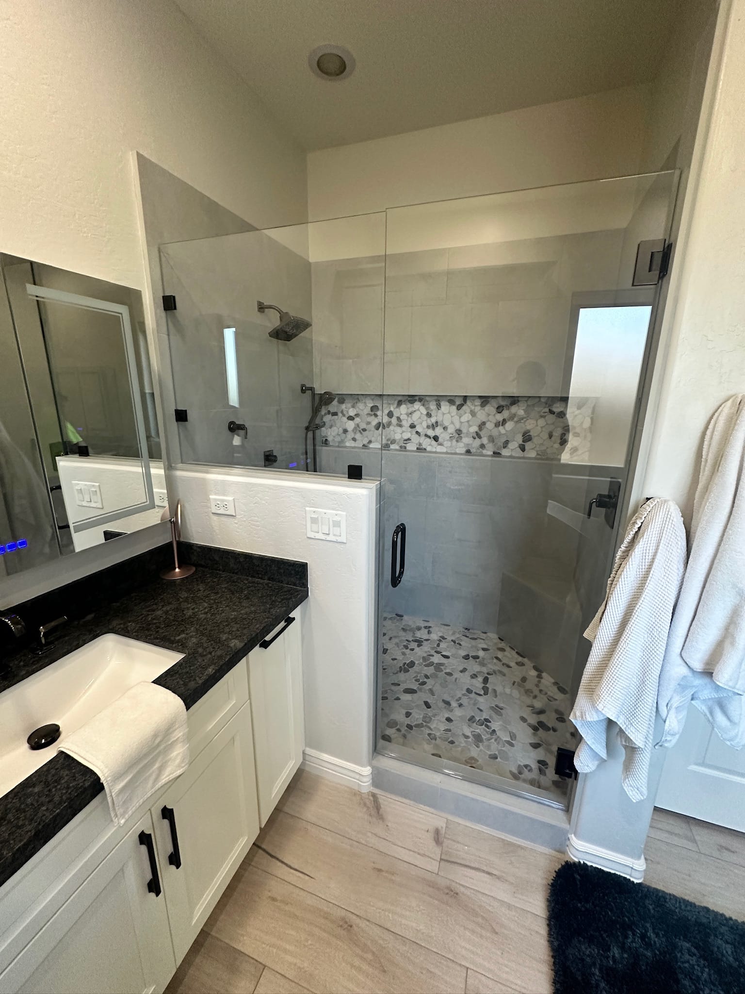 Gilbert bathroom — vanity with new walk-in shower behind, pebble mosaic niche accent, black Delta plumbing fixtures, and wood-look tile floor