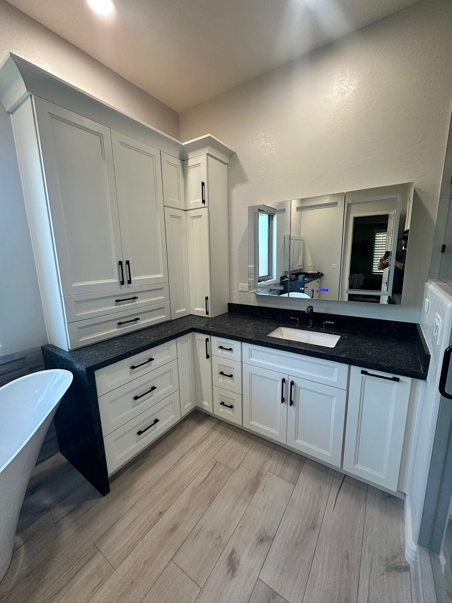 Gilbert bathroom — Sollid Monterrey Dove White shaker vanity wall with tall storage tower, waterfall black granite honed countertop, and full-wall LED lighted mirror