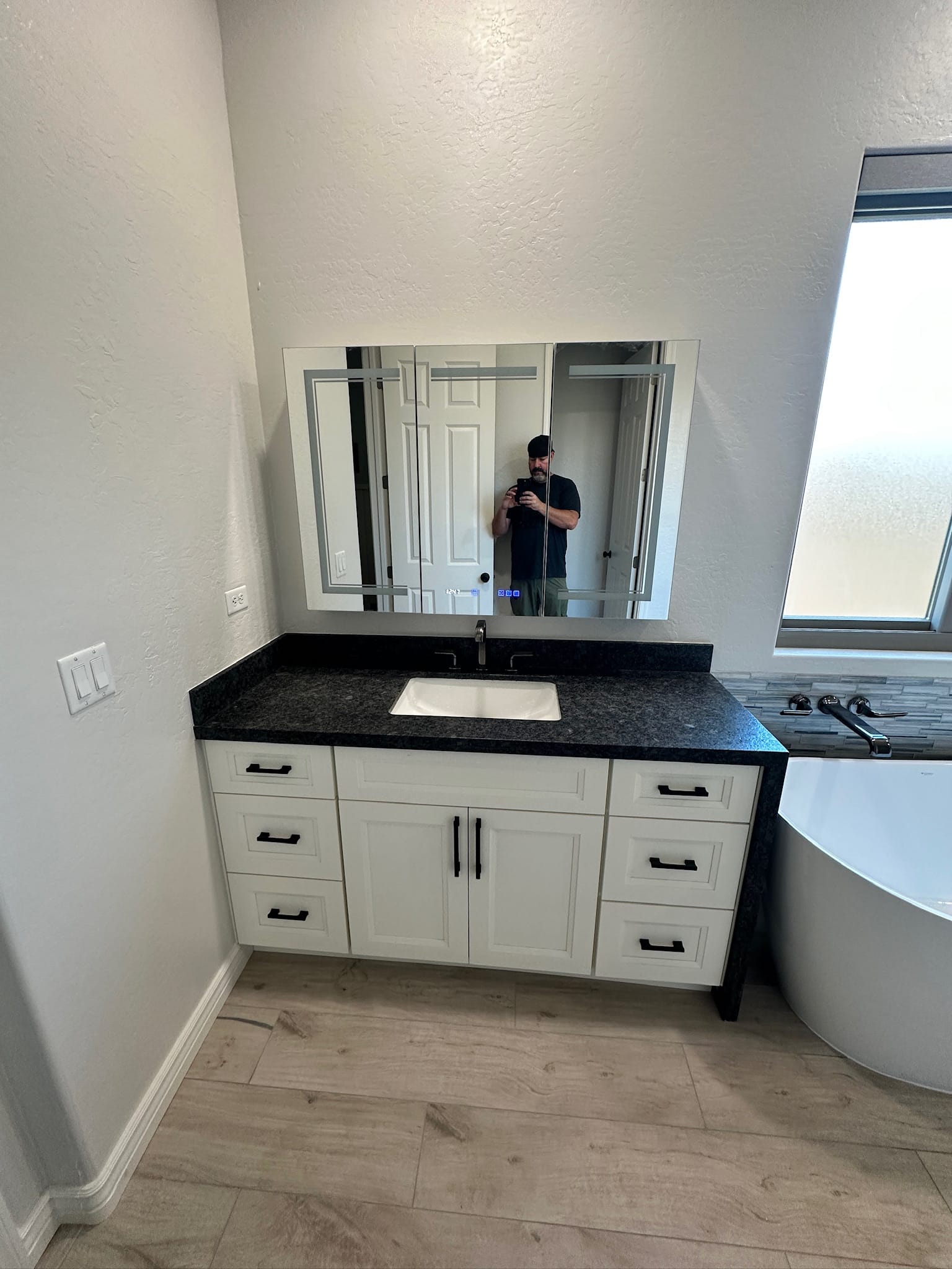 Gilbert bathroom — Sollid Monterrey Dove White vanity closeup with LED lighted mirror, black granite counter, undermount sink, and Delta black titanium faucet