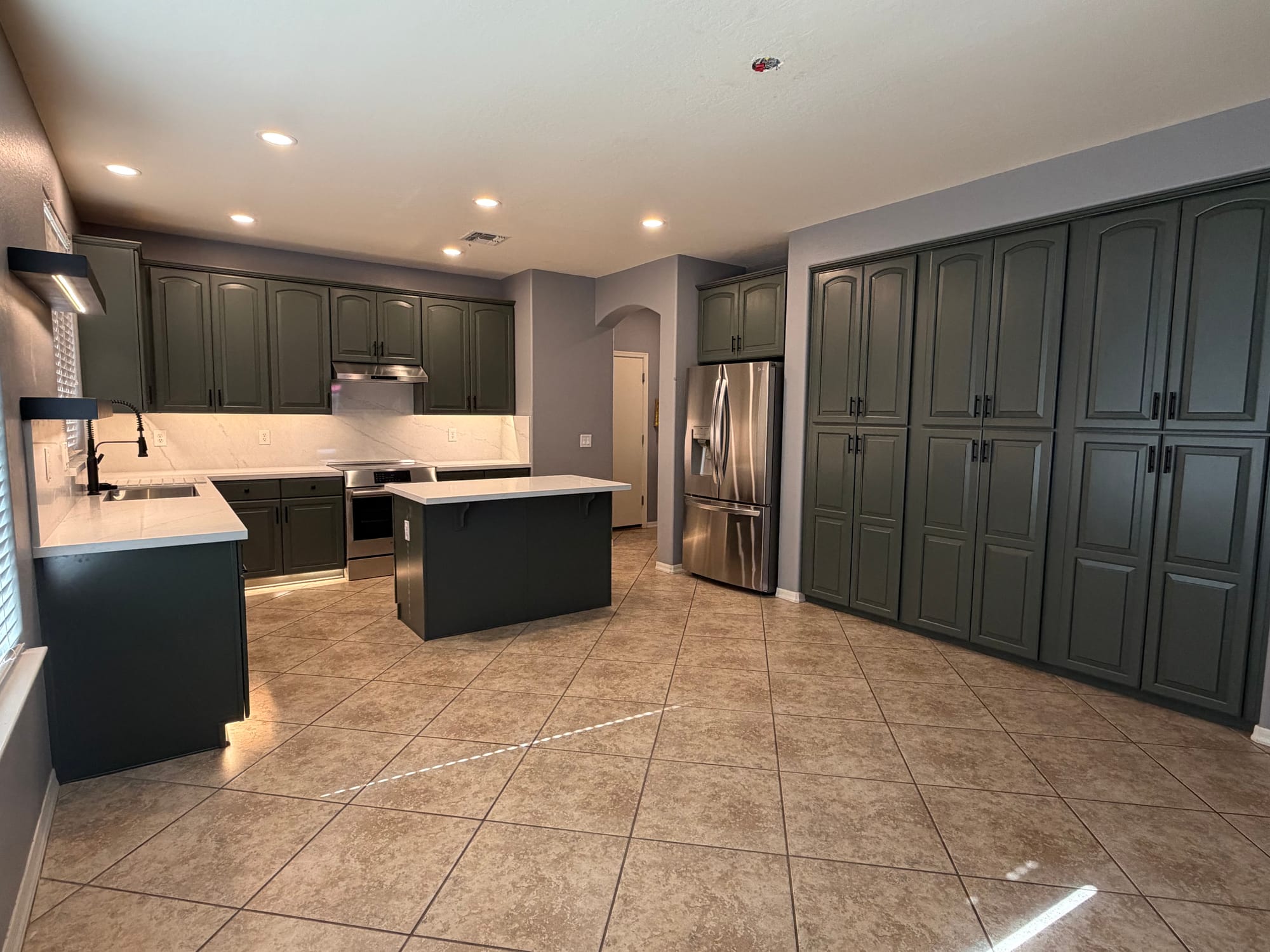 Gilbert kitchen after — modern sage cabinets, Della Terra quartz countertops and backsplash, new stainless range and hood, with Sollid black floating shelves over the sink