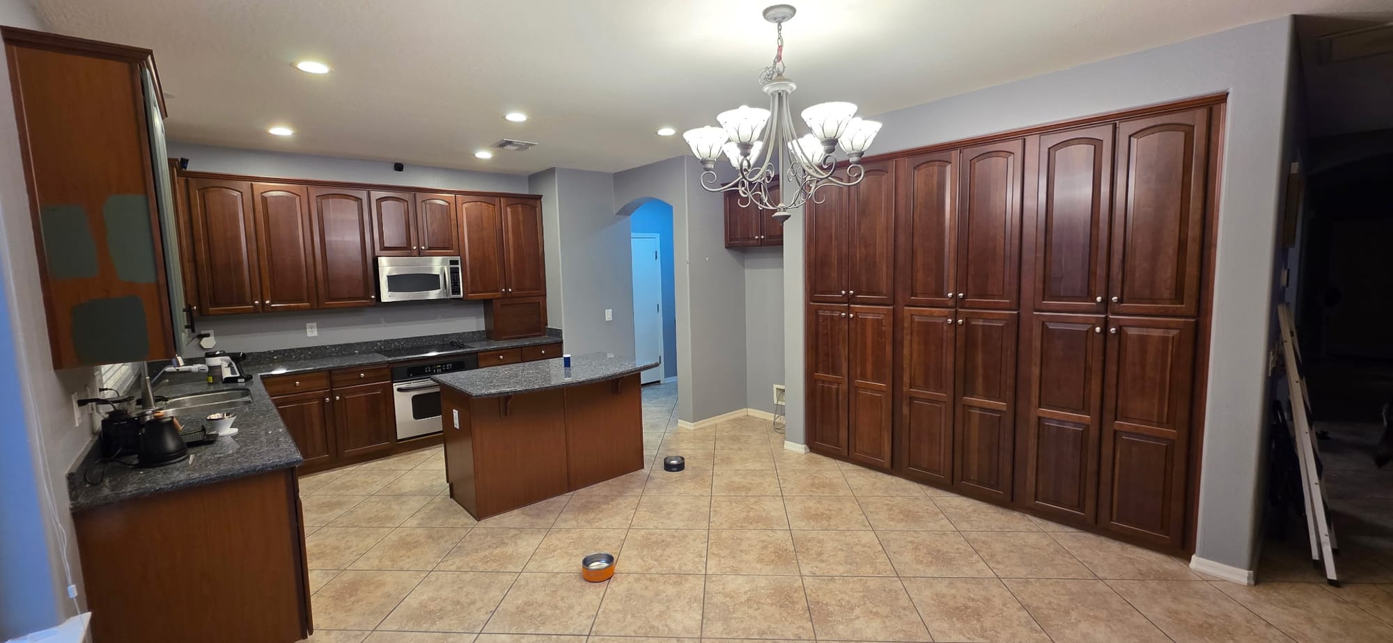 Gilbert kitchen before update — wide view of dark cherry raised-panel cabinets with chandelier and beige tile floor
