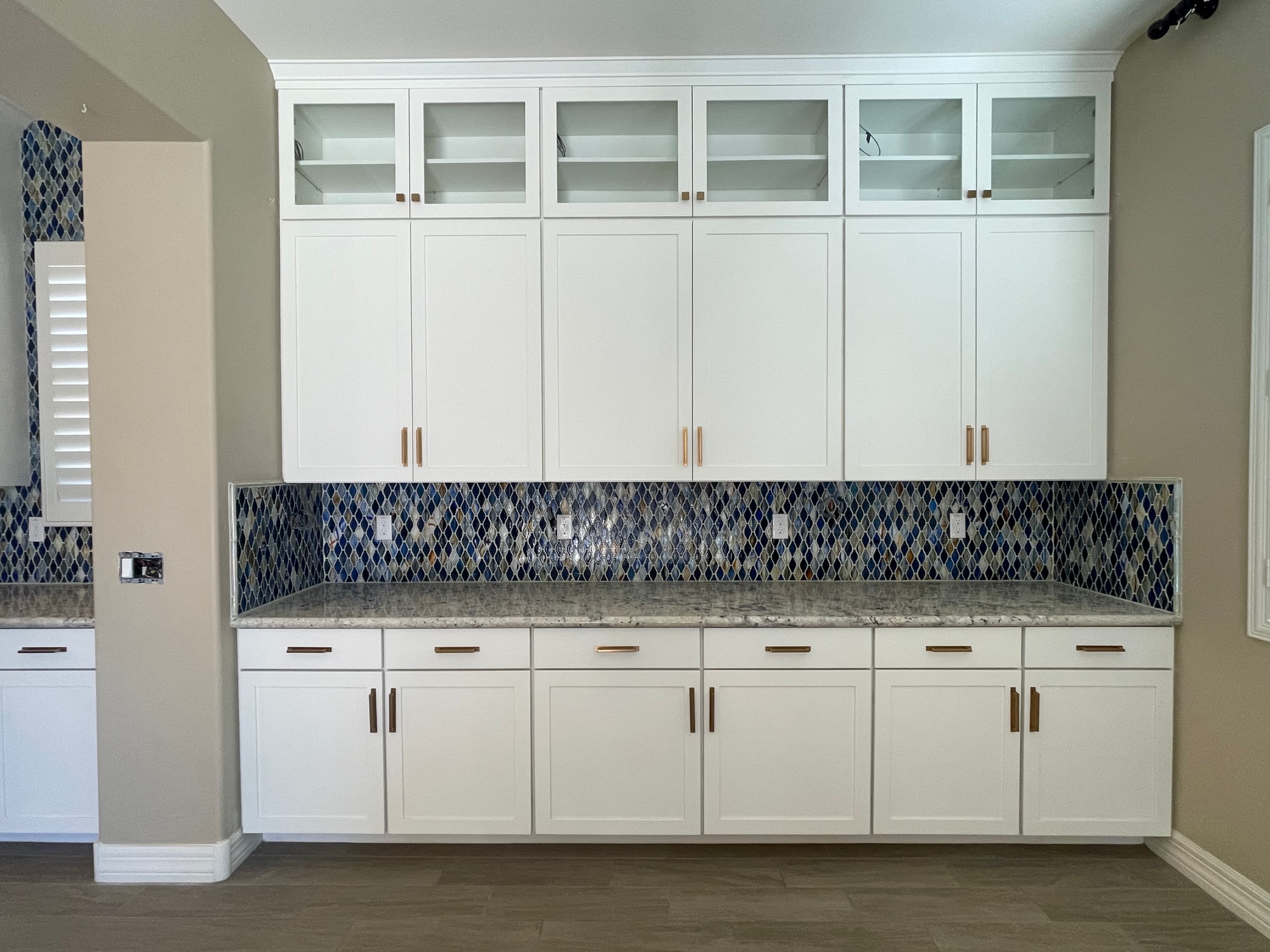 Queen Creek kitchen after — Sollid Aspen Dove White cabinetry extended to the ceiling on the hutch wall, top tier is glass display with in-cabinet LED lighting, gold bar pulls, and the existing blue mosaic backsplash carried all the way up to the new cabinets