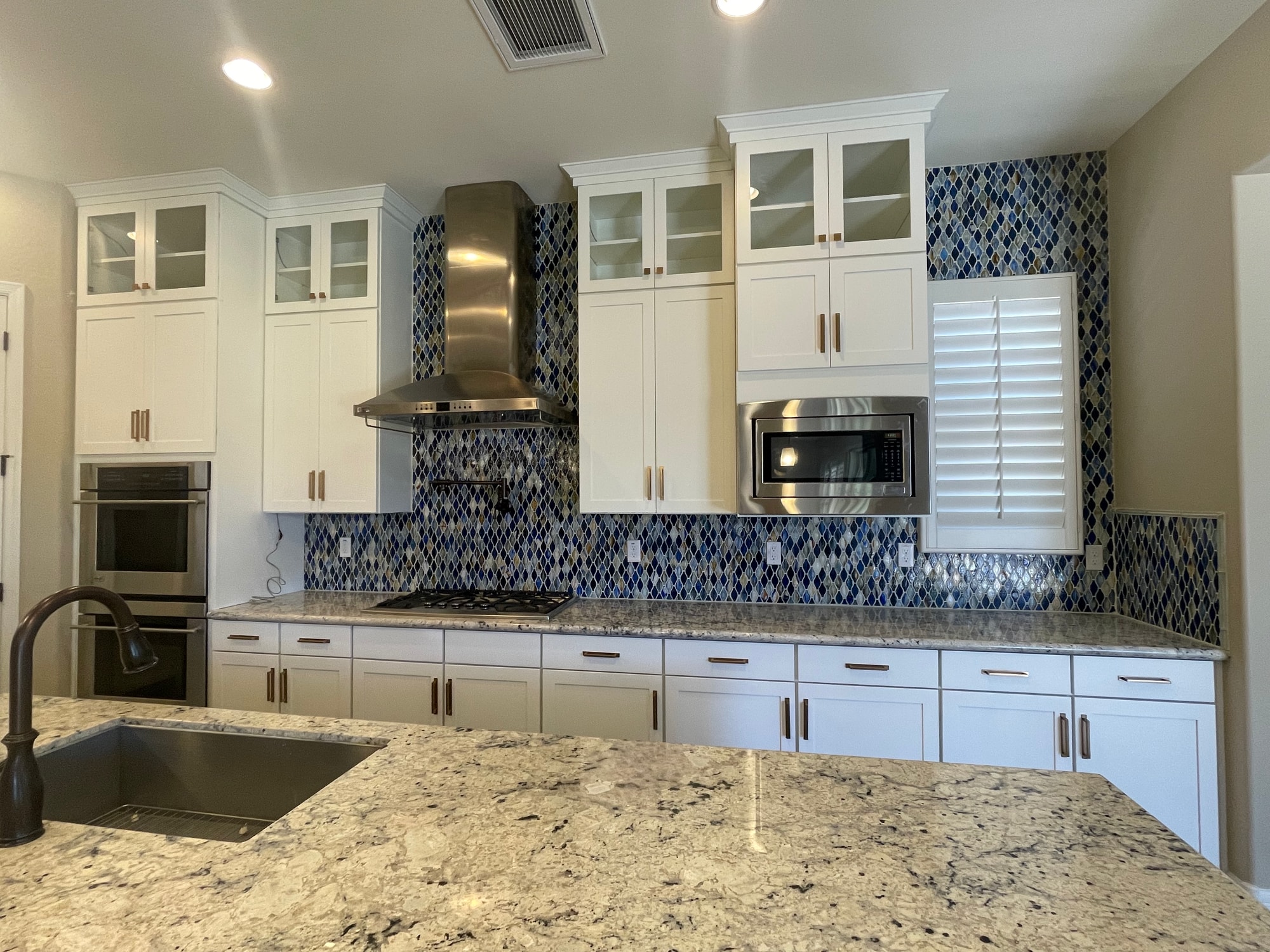 Queen Creek kitchen after — main cook wall with uniform-height Sollid Aspen Dove White uppers extended to the ceiling, glass display cabinets on top with LED strip lighting, gold bar pulls, and the mosaic backsplash extended up to meet the new cabinets