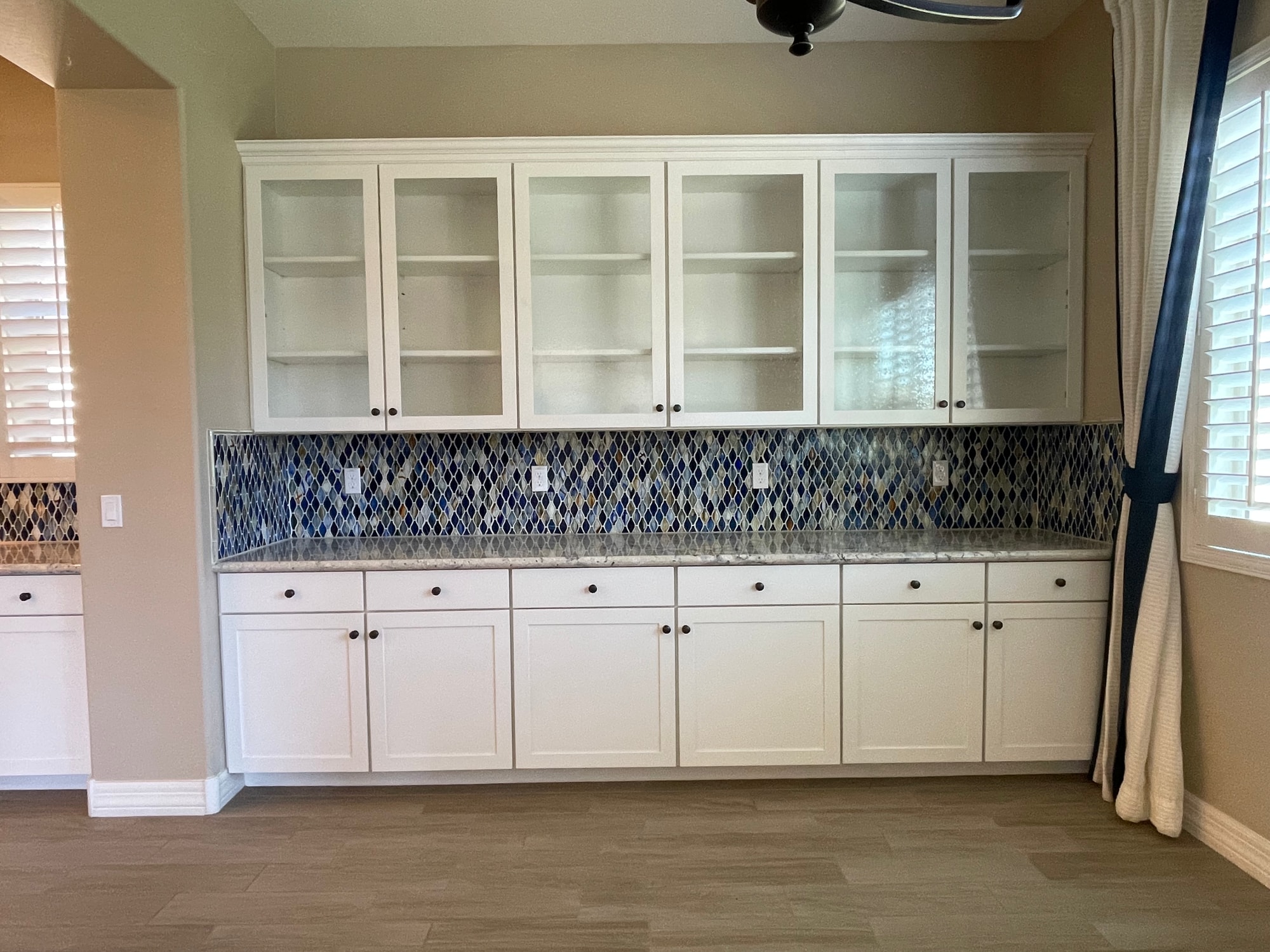 Queen Creek kitchen before — white hutch/buffet wall with short upper cabinets stopping well below the ceiling, dark bronze knob hardware, existing blue mosaic backsplash between the granite counters and the uppers