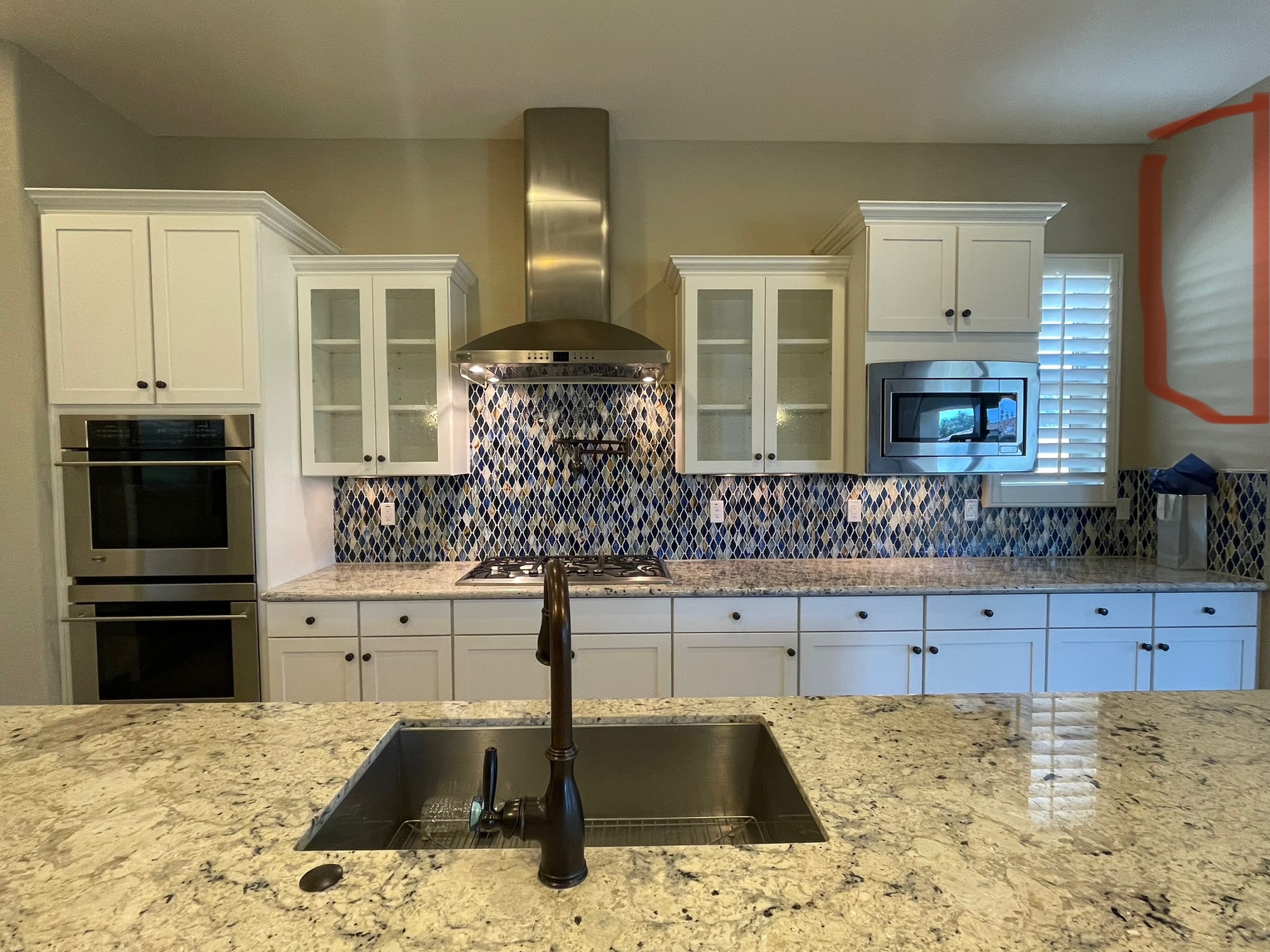 Queen Creek kitchen before — main cook wall with mismatched-height uppers around the stainless range hood, existing granite countertops on the island, blue mosaic backsplash stopping short of the shorter uppers