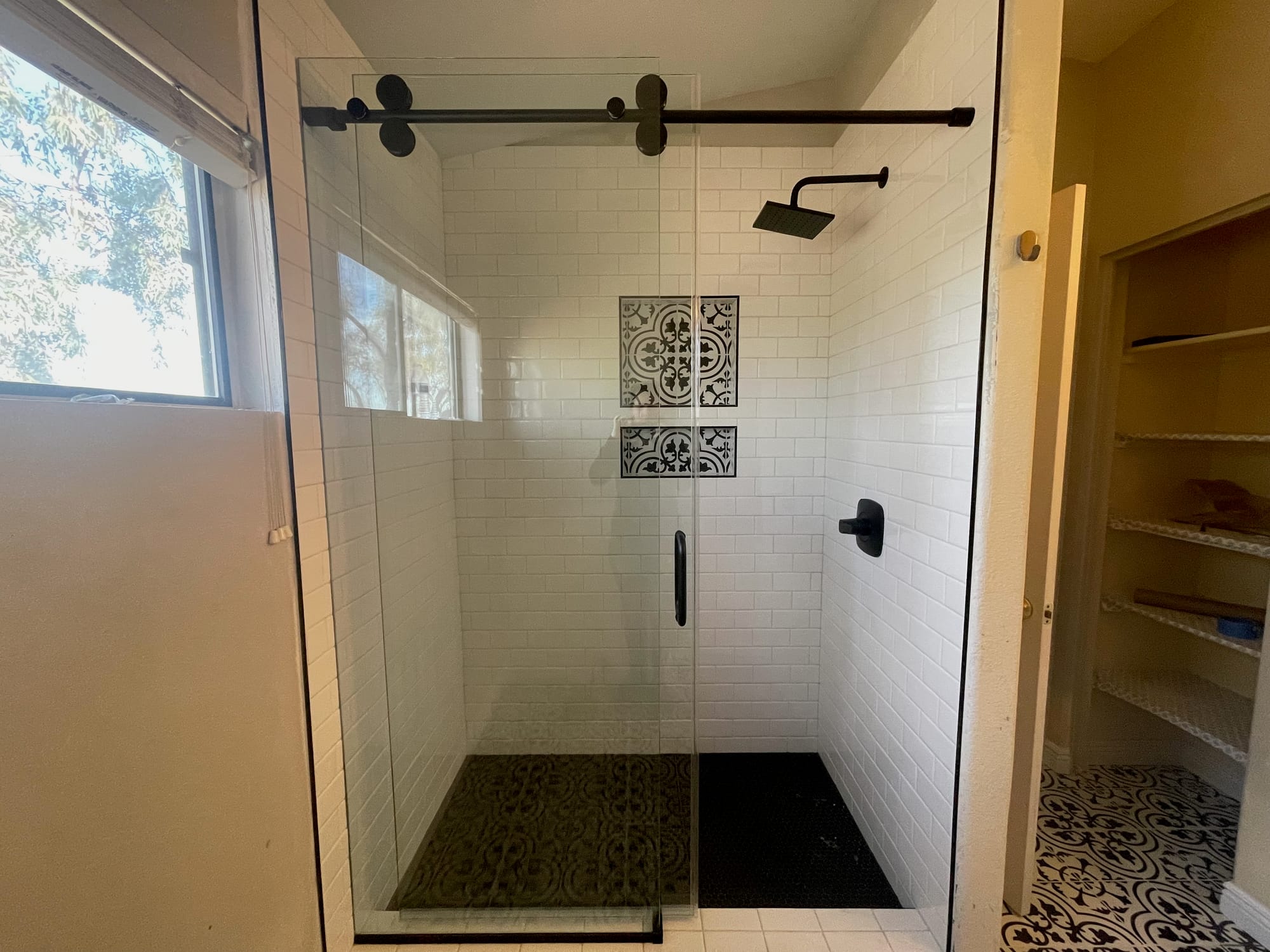 Scottsdale master bathroom after — custom walk-in white subway tile shower with matte black sliding glass door, patterned cement-tile niches, black hexagon mosaic shower floor, and the built-in linen shelving preserved to the right
